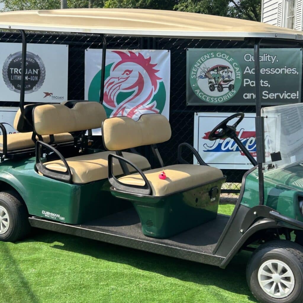 Green Cushman Shuttle 6 golf cart with extended roof and tan seats, featuring Stenten's Golf Cart Accessories signage.